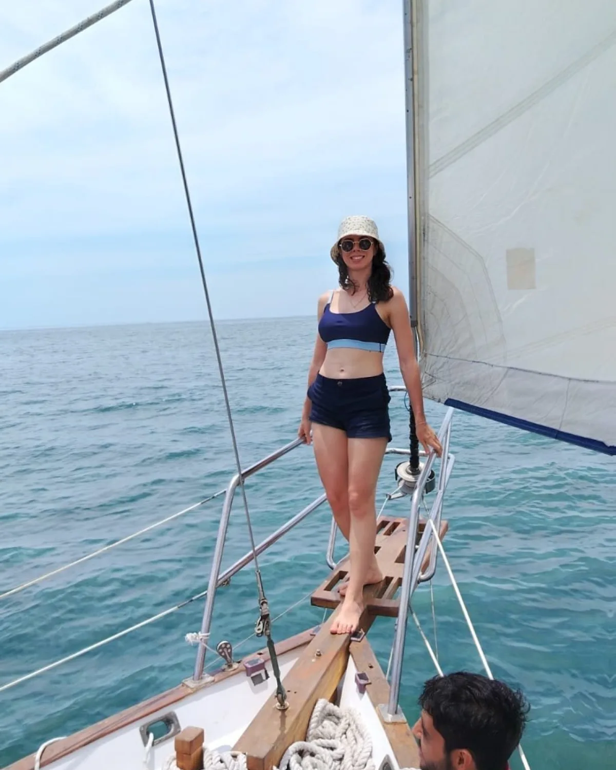 Invitada de pie en la proa del velero Down East 38 con la vela desplegada sobre la Bahía de Banderas